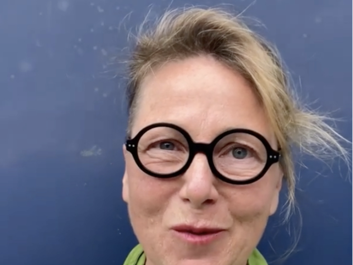 Photograph of a woman with blonde hair, round black glasses and a green shirt