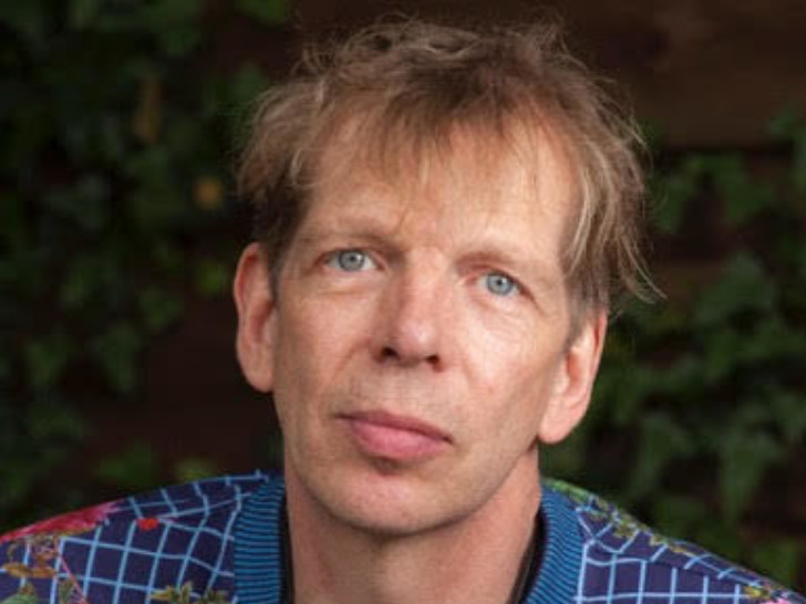 David Hoyle looking at the camera with a neutral facial expression, wearing a floral crewneck jumper.