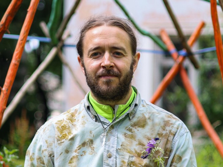 Headshot of Sean Roy Parker stood outdoors with flowers in his pocket.