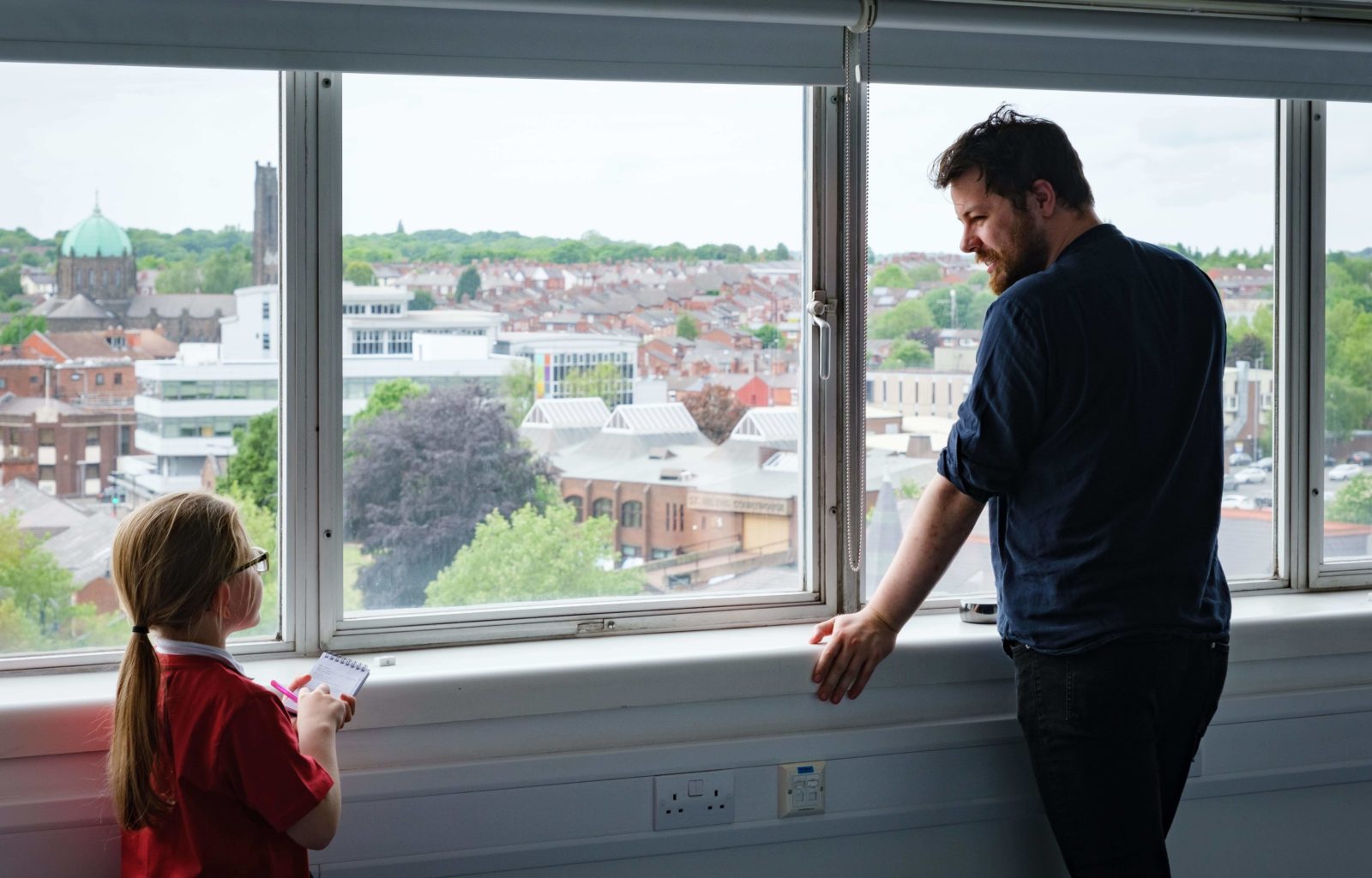 A man and a child talking in front of the windows.