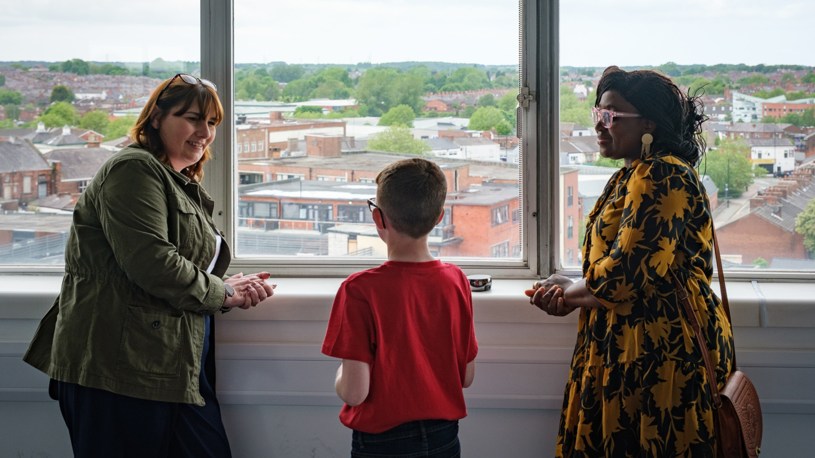 Photograph of 2 women having a conversation with a schoolboy in front of a window that looks over St Helens.