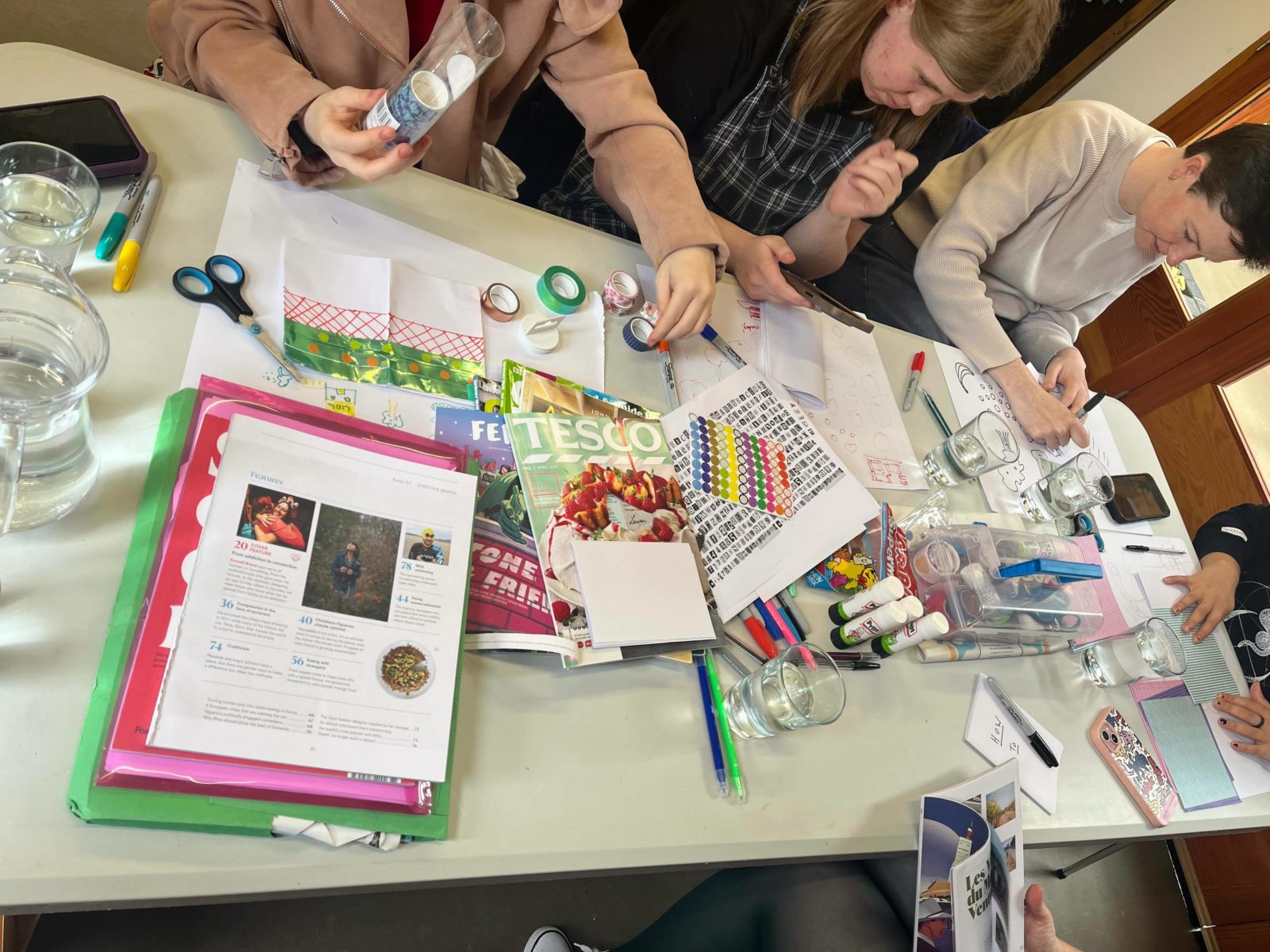 People sat around a table full of craft materials making zines