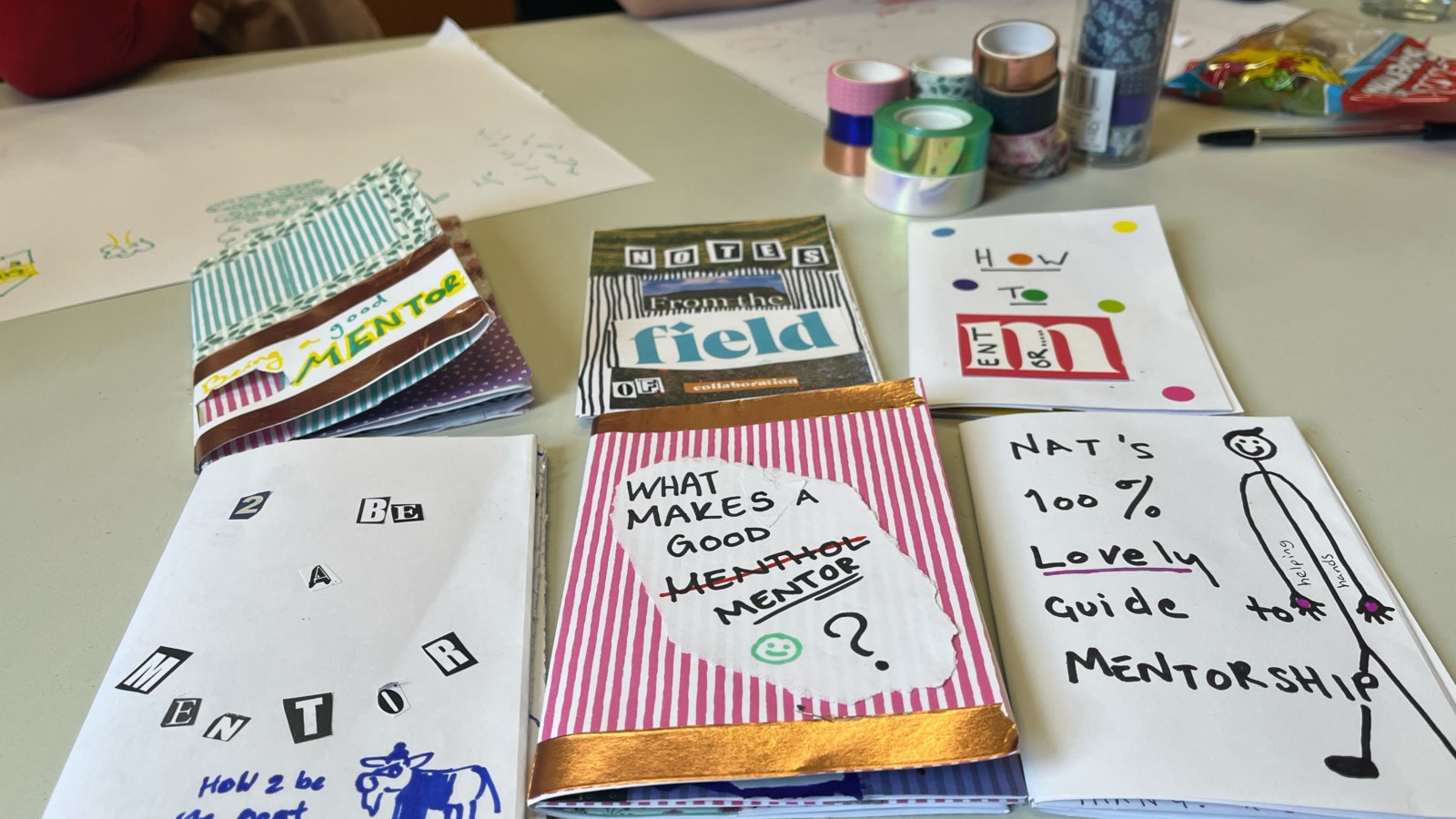 6 zines are laid out on a table, they are named things such as 'how 2 be the goat’, ‘nat’s 100% lovely guide to mentorship’, ‘How to mentor’, ‘notes from the field of collaboration’ and ‘being a good mentor’. They are all hand made using materials such as collage and marker pen.