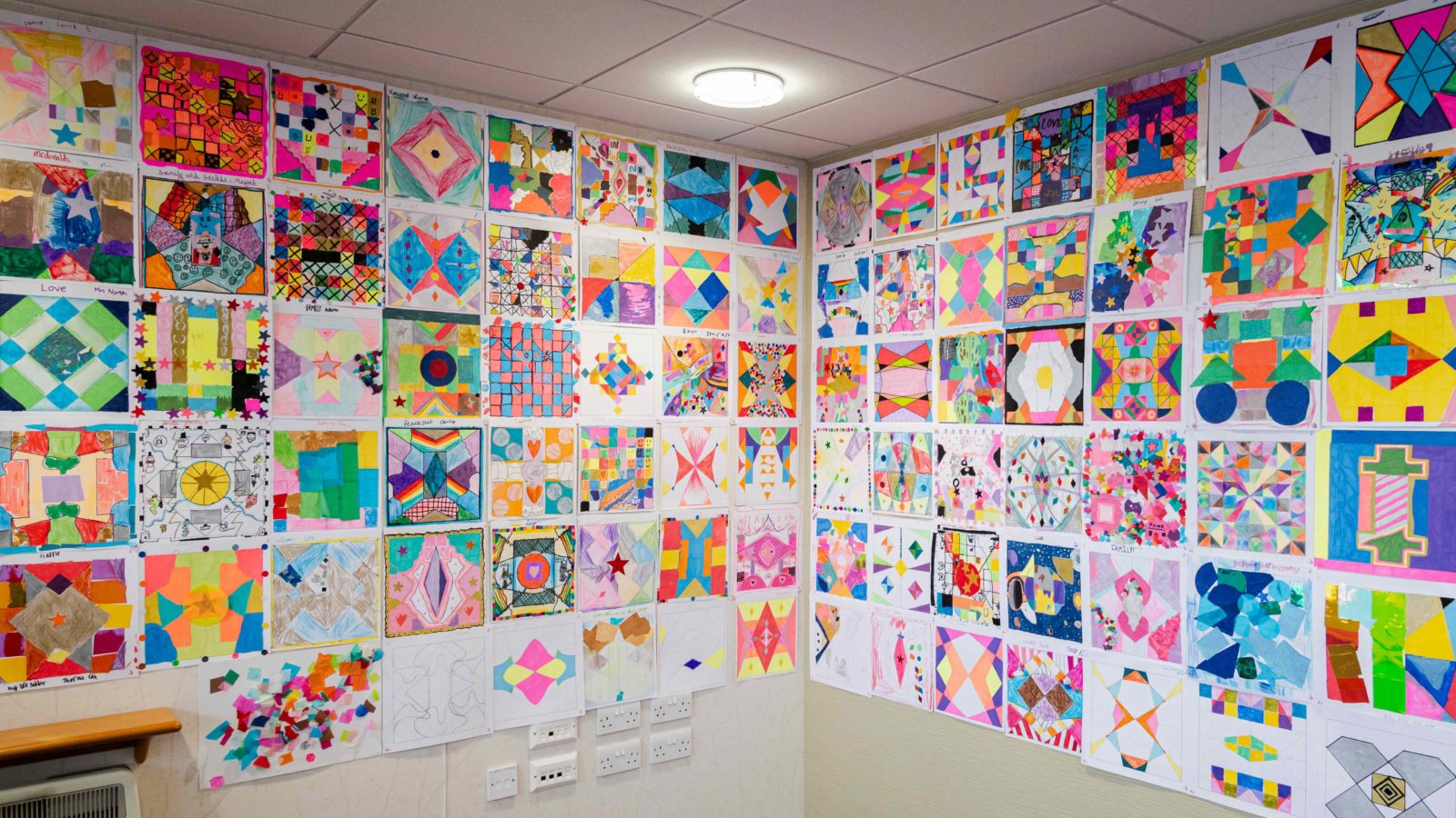 a wall full of the peace patterns that the Stockbridge community created for the mural. They are all vibrant, symmetrical patterns, some with glitter and stickers on them.