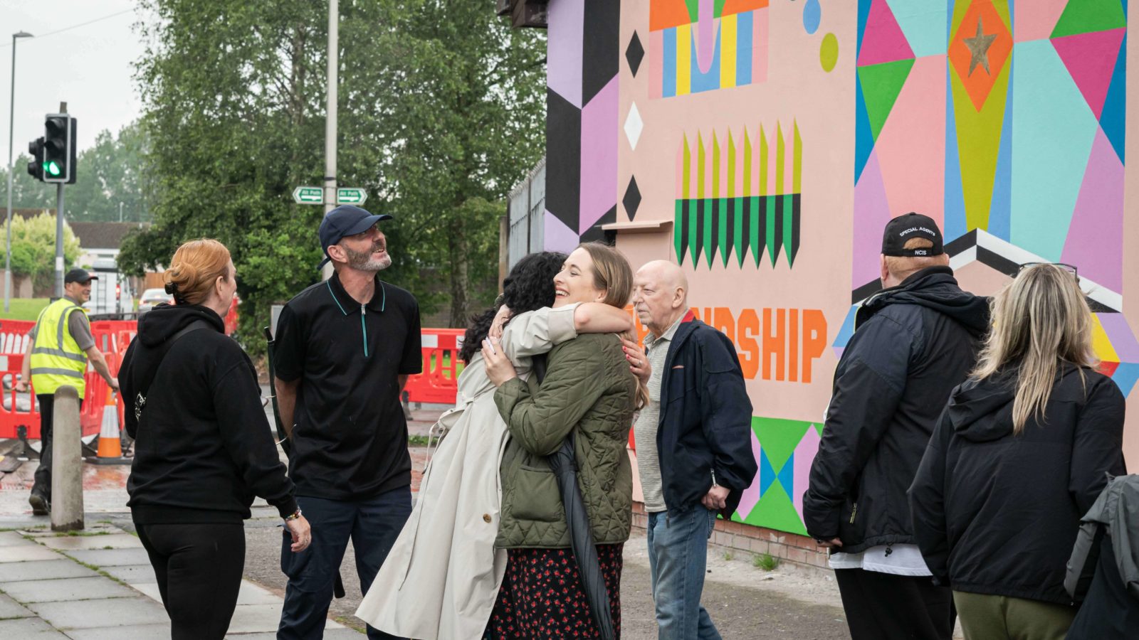 People are photographed candidly standing in front of the mural, Cherie hugs Heart of Glass producer Rhyannon.