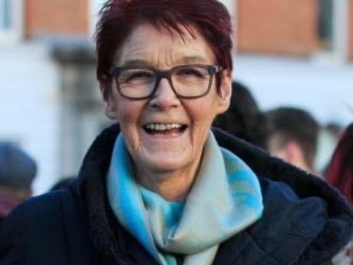 Photograph of a woman with short, auburn hair, square glasses and a banner which says "repeal"