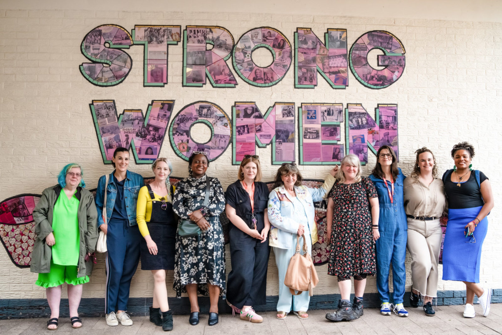 10 women smile for the camera stood in front of the mural.
