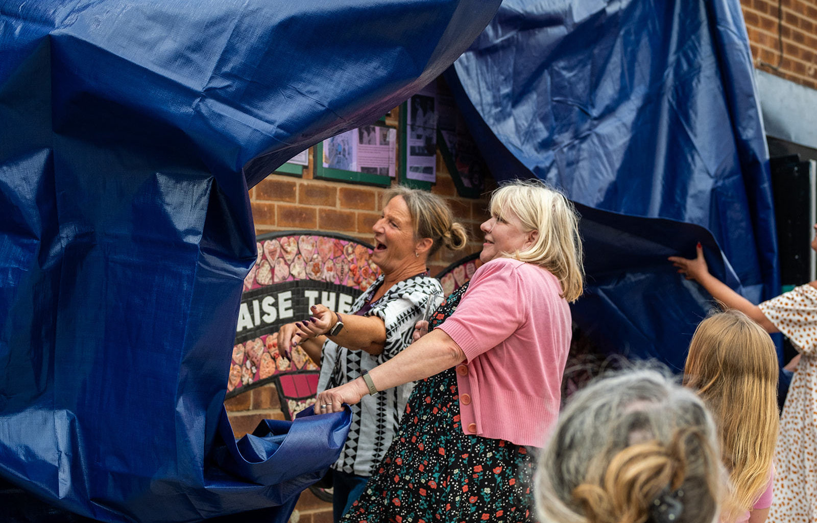 Carrie and a member of the St Helens community tear away the dark blue tarpaulin to reveal the mural.