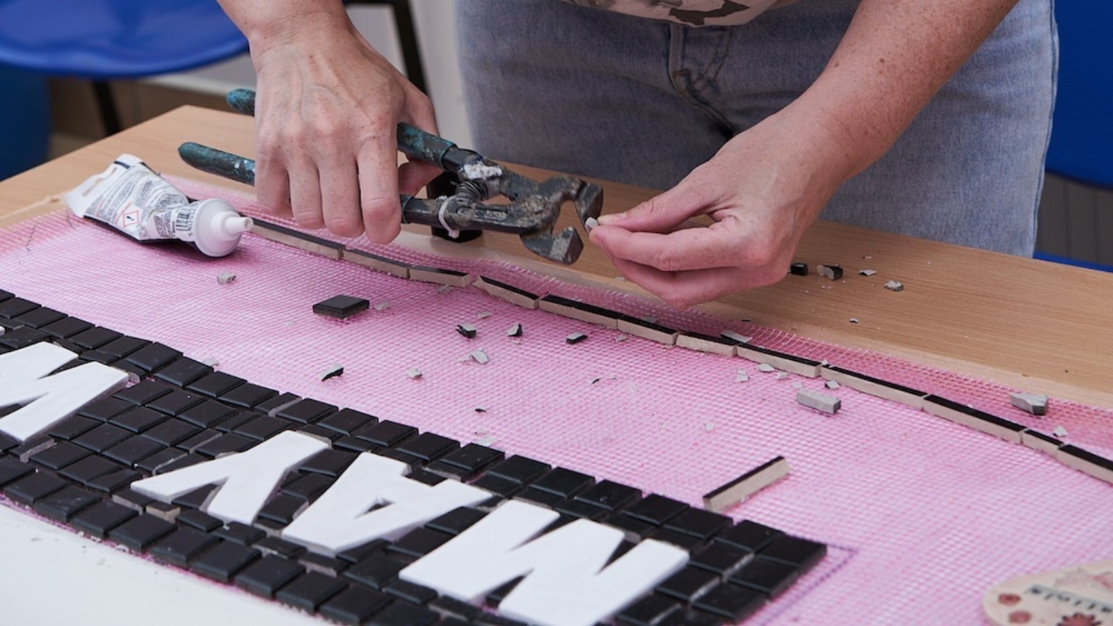 A woman uses tools to cut and place mosaic tiles