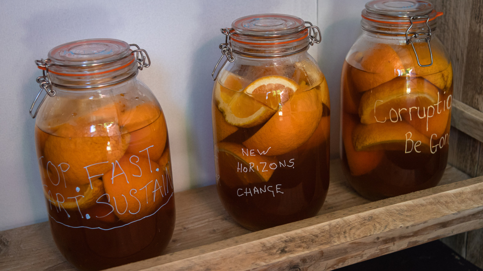 A row of glass jars on a shelf, each containing fruit and liquid