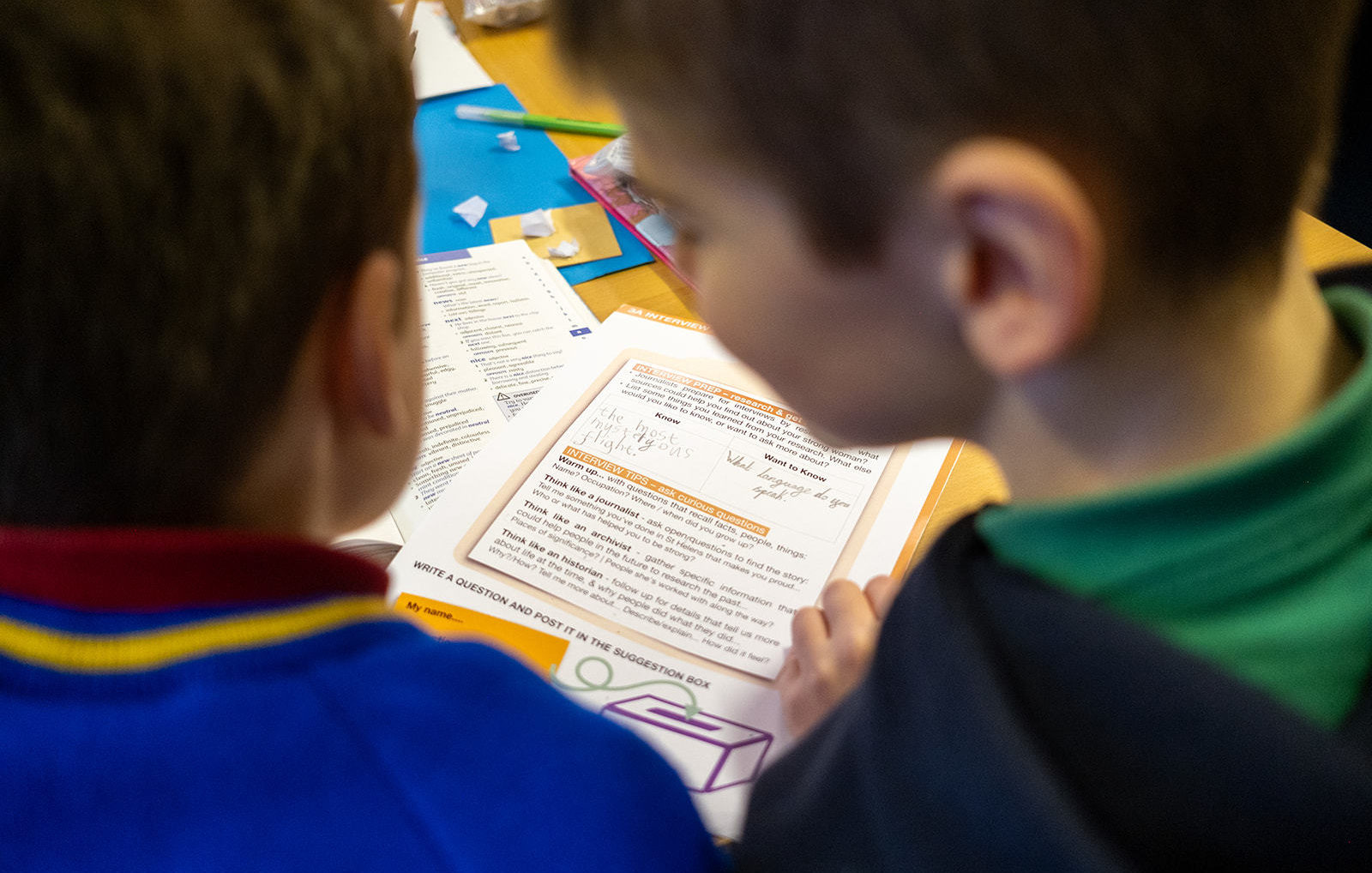 Two schoolchildren are photographed from the shoulders up from behind, between their heads the resource can be seen on the table.