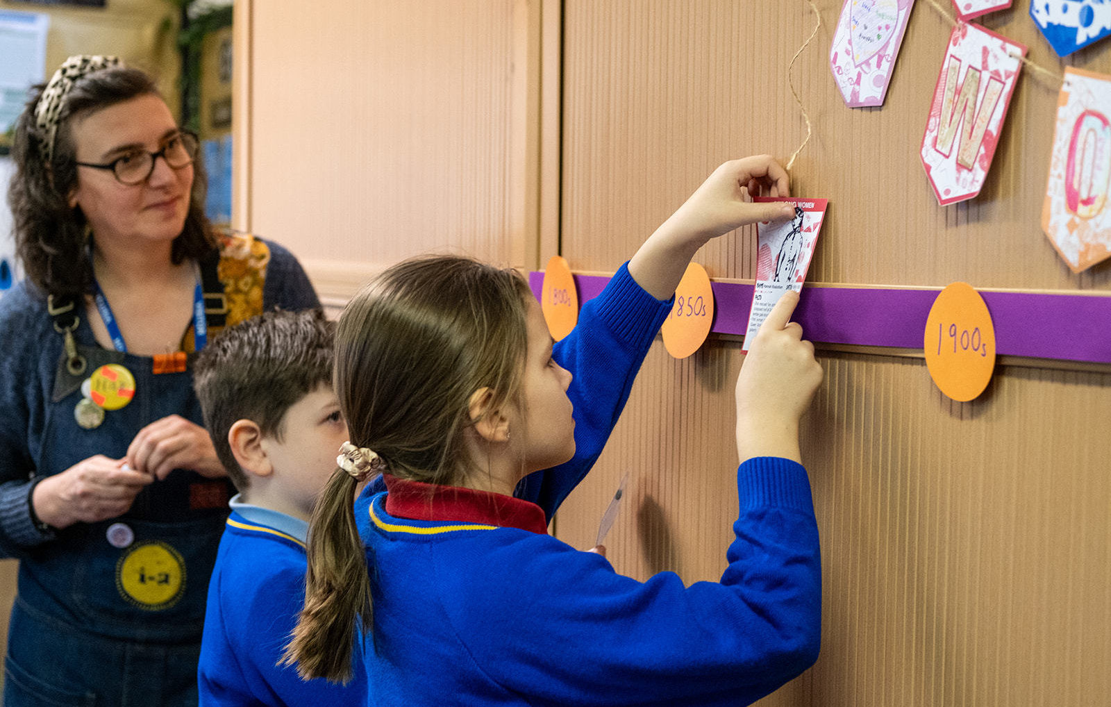 A schoolgirl pins a card with an illustration and words about a woman on a timeline.