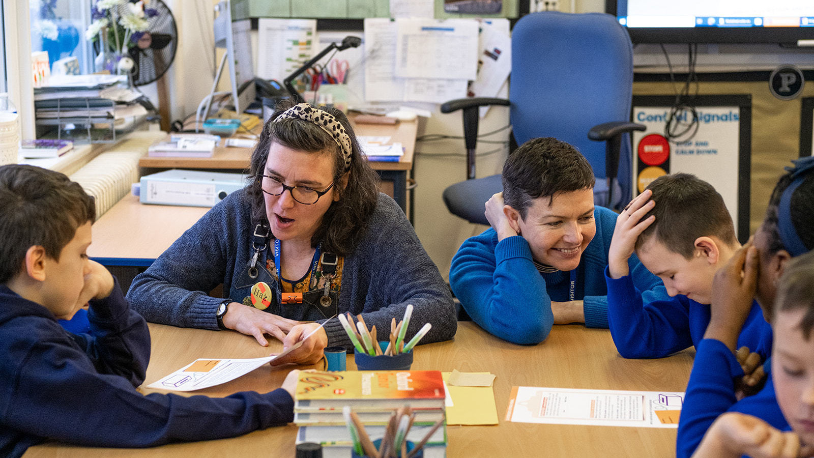 schoolkids in blue uniform sit around a table laughing whilst going through the schools resource with heart of glass producer Nat and Interference art's Maura.