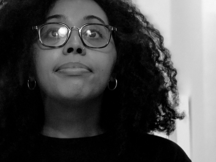 Photograph of a black woman with wavy natural hair, wearing glasses