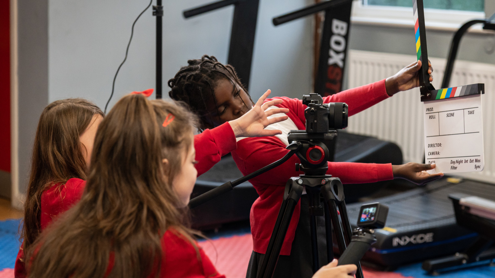 Photograph of a group of children wearing red school uniforms, using a go pro and other film equipment