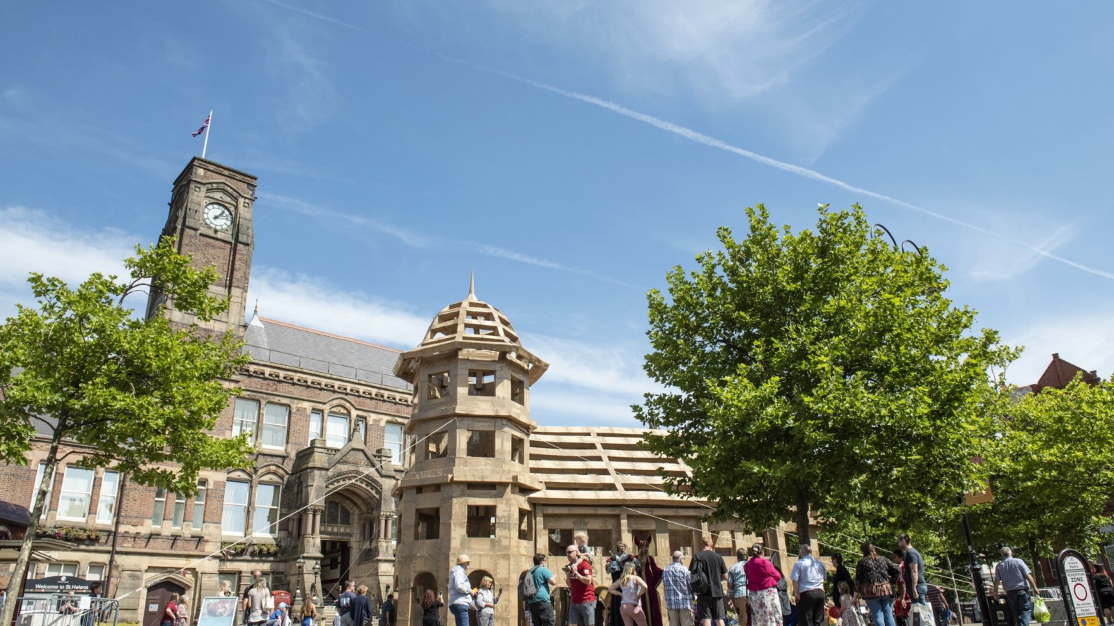 A large cardboard castle is photographed in front of St Helens Town Hall on a sunny day. People gather to look at it.